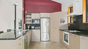 A modern kitchen with a stainless steel refrigerator, a microwave, and a stove. There is a dining area with a table and chairs. - Edgewater Escape - Cromwell Holiday Home (Cromwell)