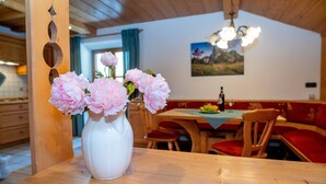 Ein Holzespeisesaal mit einer weißen Vase voller rosa Blumen, Holzsesseln und einer roten gepolsterten Bank in einem Raum mit Holzbalkendecken und einem Gemälde an der Wand.