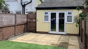 A small house with a tiled patio, a grassy lawn, and a wooden fence. - House - Sleeps 5 - Pet Friendly - West Facing Enclosed Rear Garden - On Street Parking (Lytham St. Anne's)