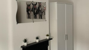 A room with a black fireplace, three small potted plants on the mantel, a white wardrobe, and a framed artwork of donkeys on the wall. - House - Sleeps 5 - Pet Friendly - West Facing Enclosed Rear Garden - On Street Parking (Lytham St. Anne's)