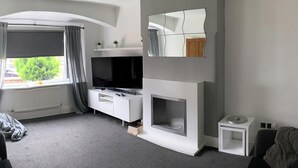 A modern living room with a fireplace, a flat-screen TV, and a large window with curtains. - House - Sleeps 5 - Pet Friendly - West Facing Enclosed Rear Garden - On Street Parking (Lytham St. Anne's)