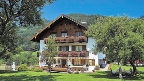 A two-story chalet with a wooden facade, balconies with flower boxes, and a well-maintained lawn. - Vacation apartment Watzmo, 1-3 persons, 50 sqm, balcony, separate bedroom (Ramsau bei Berchtesgaden)