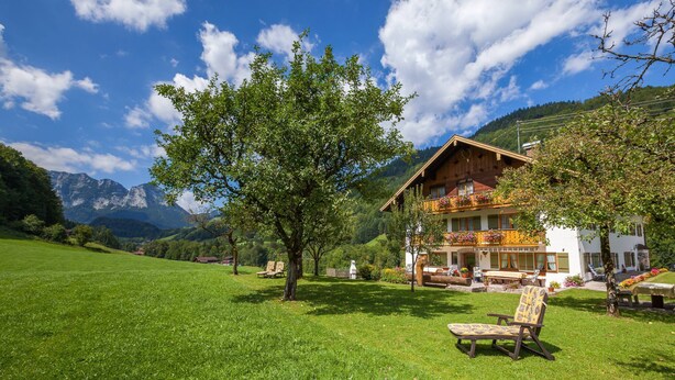 A chalet with a balcony, surrounded by a lush green lawn and a mountain backdrop. - Vacation apartment Watzmo, 1-3 persons, 50 sqm, balcony, separate bedroom (Ramsau bei Berchtesgaden)