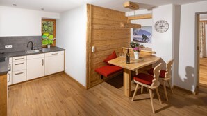 A modern kitchen with a wooden wall, a dining area with a wooden table and chairs, and a window with a view of greenery. - Vacation apartment Watzmo, 1-3 persons, 50 sqm, balcony, separate bedroom (Ramsau bei Berchtesgaden)