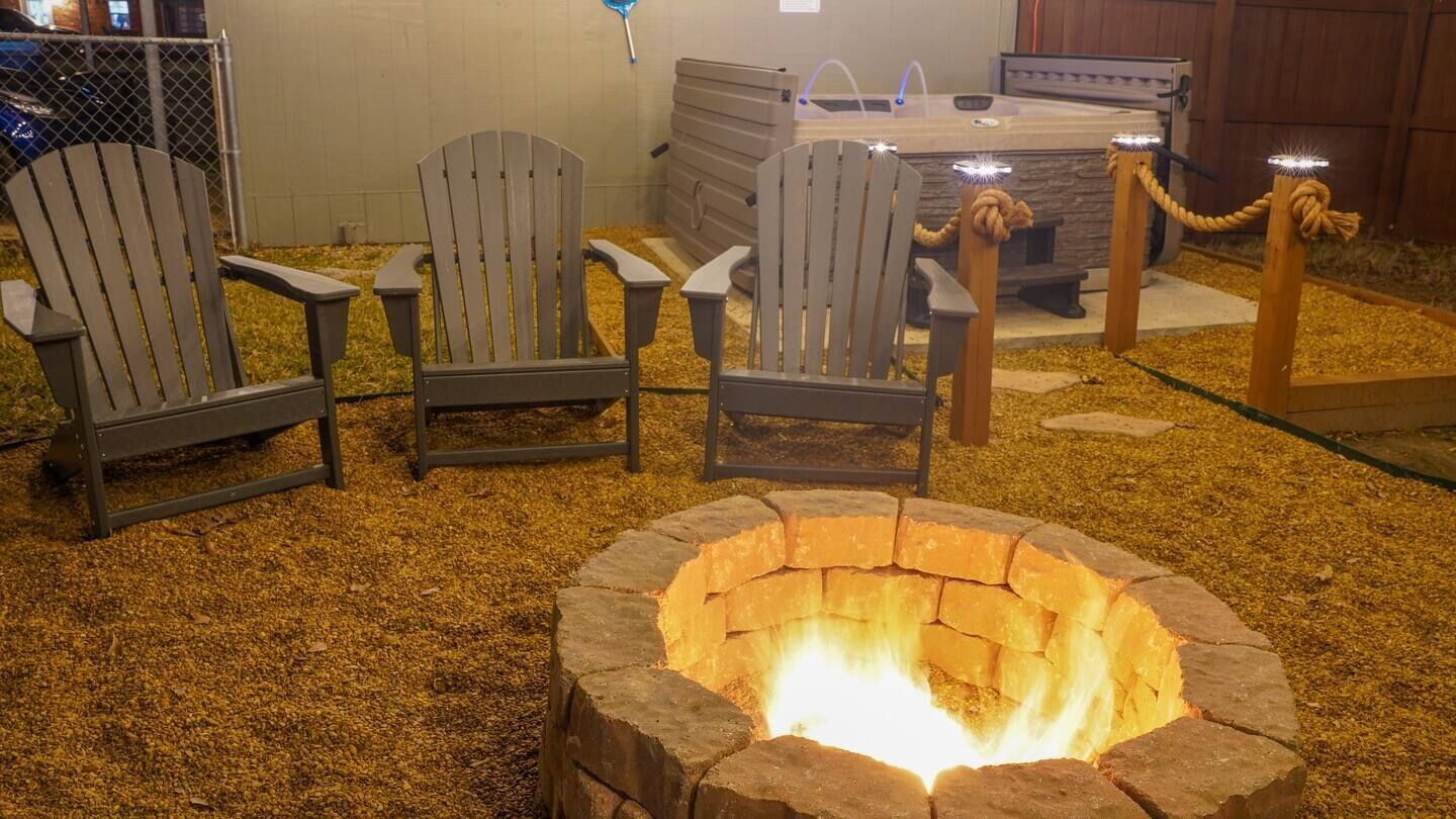 A fire pit surrounded by Adirondack chairs, a hot tub, and a wooden deck.