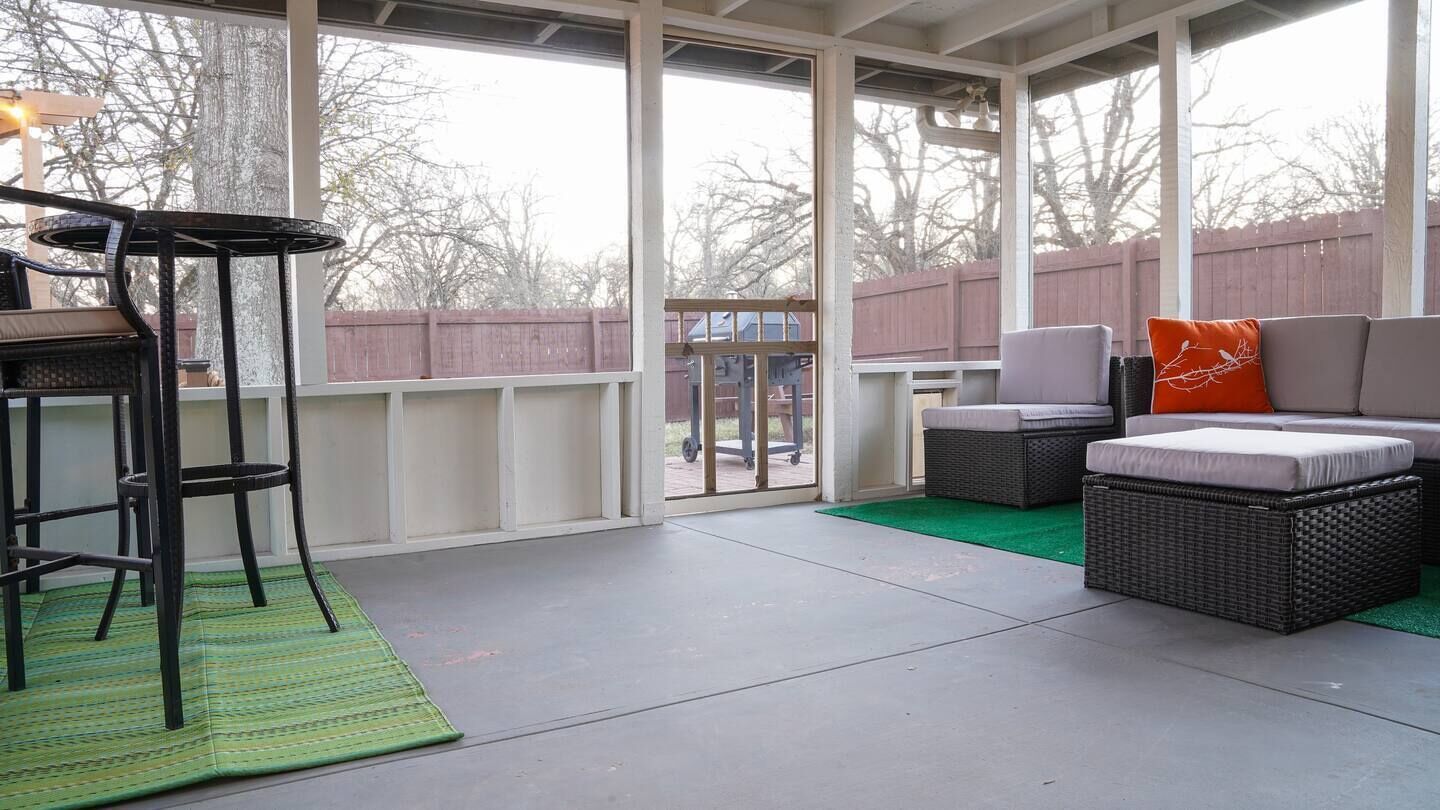 Un patio couvert comprenant un bar avec des tabourets, des meubles en osier et une vue sur le jardin à travers de grandes fenêtres.
