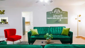 A modern living room with a green sofa, a red armchair, and a coffee table. A welcome sign to TROPPO CASA ON LAKE SIDE is visible on the wall.