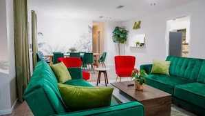 A modern living room with green sofas, a red chair, and a dining area with green chairs.