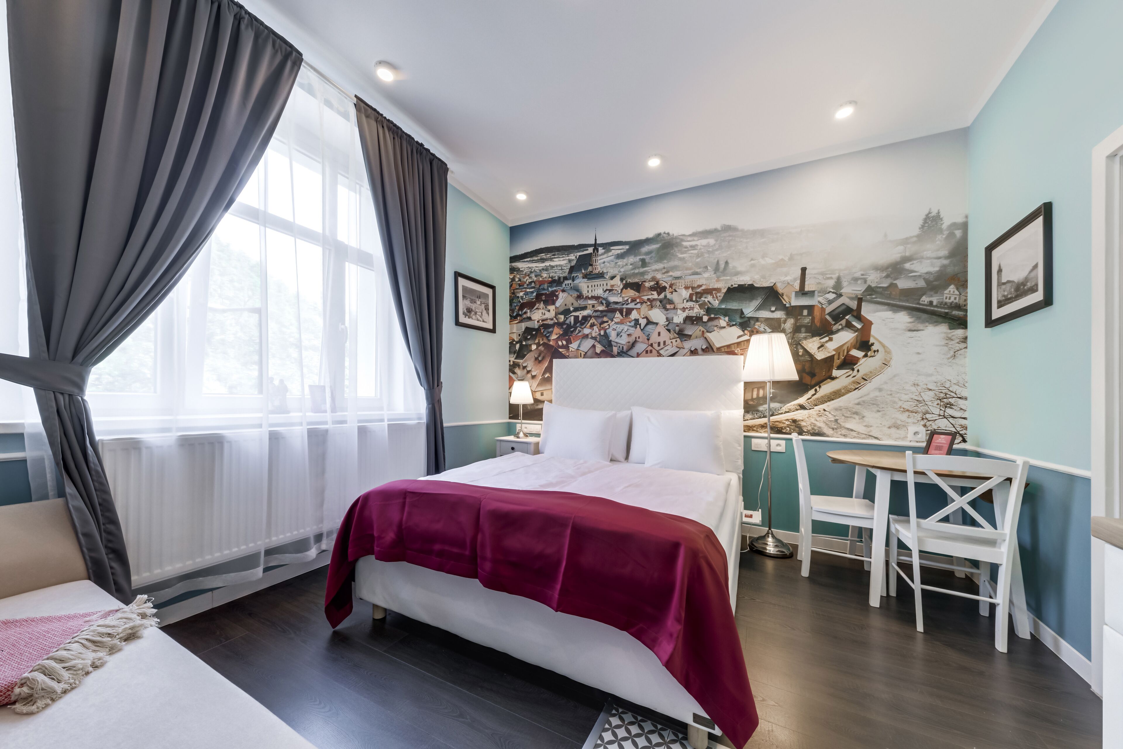 Habitación de hotel con una cama grande, un escritorio con silla, vistas a un mural urbano y una ventana con cortinas.