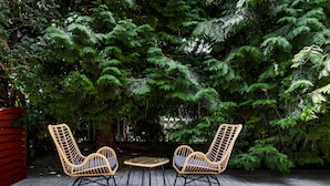 A patio with two wicker chairs and a small table, surrounded by dense green foliage. - Revelton Studios Prague (Prague)