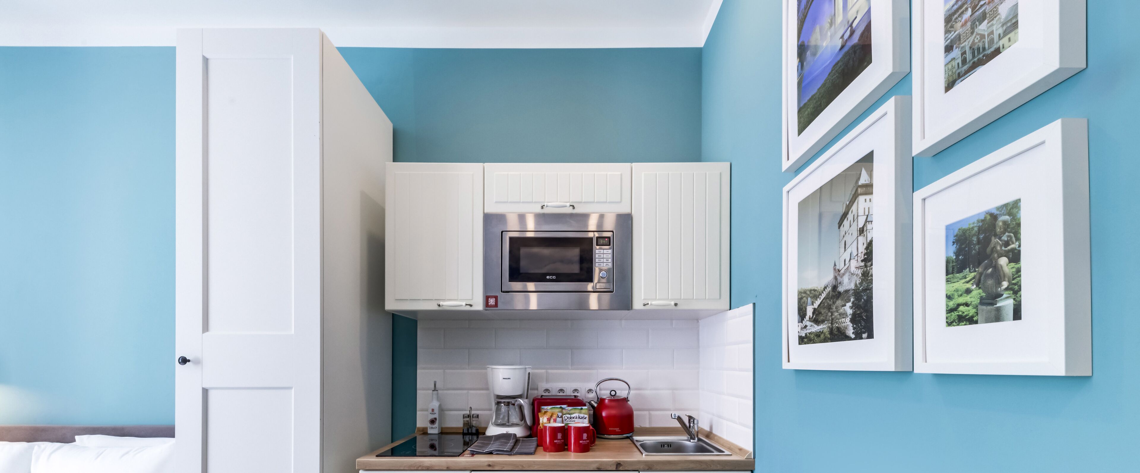 Una cocina compacta con armarios blancos, microondas integrado, cafetera y tostadora.