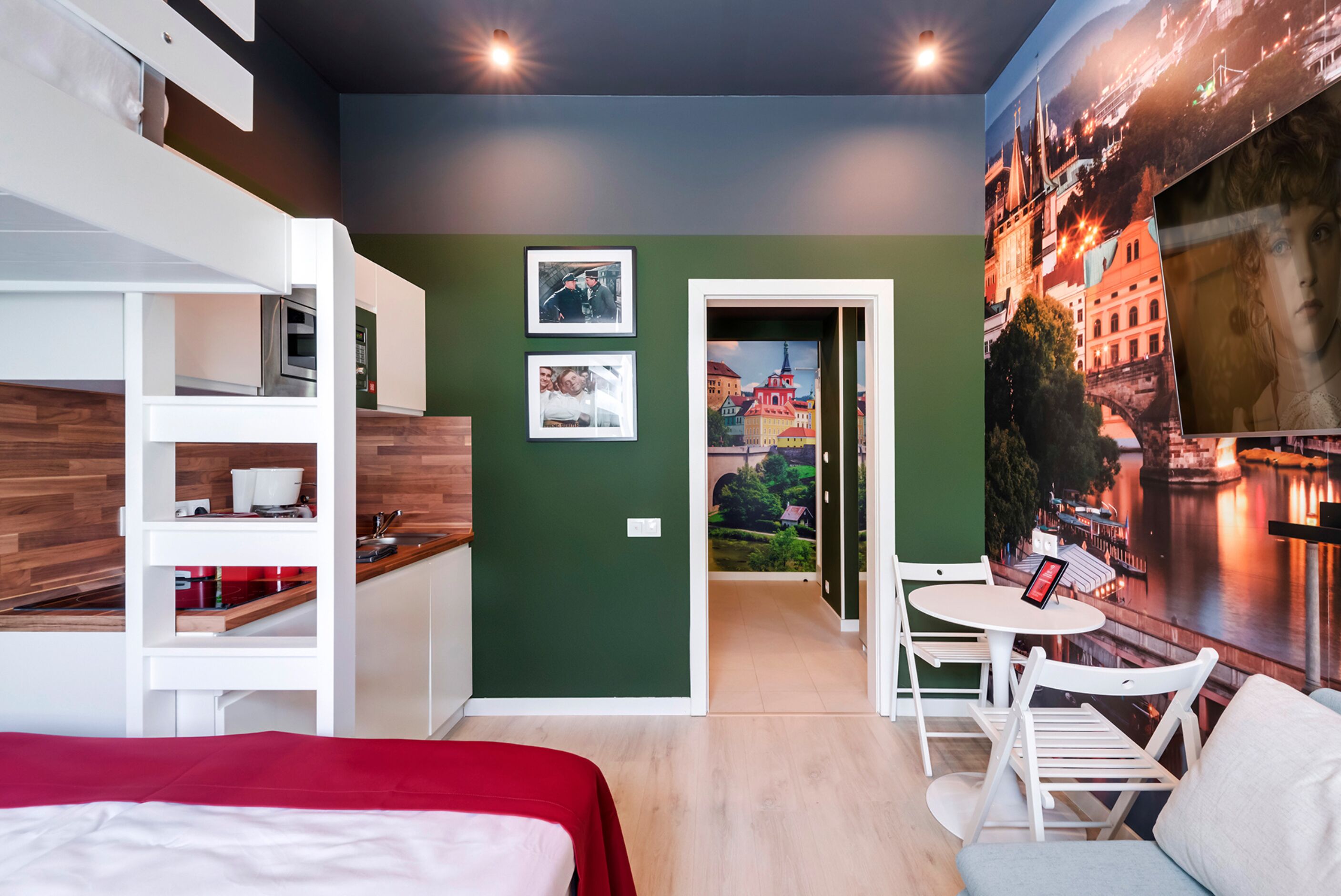 Ein modernes Hotelzimmer mit Bett, Küchenzeile, Essbereich und einem Stadtbild-Wandbild.
