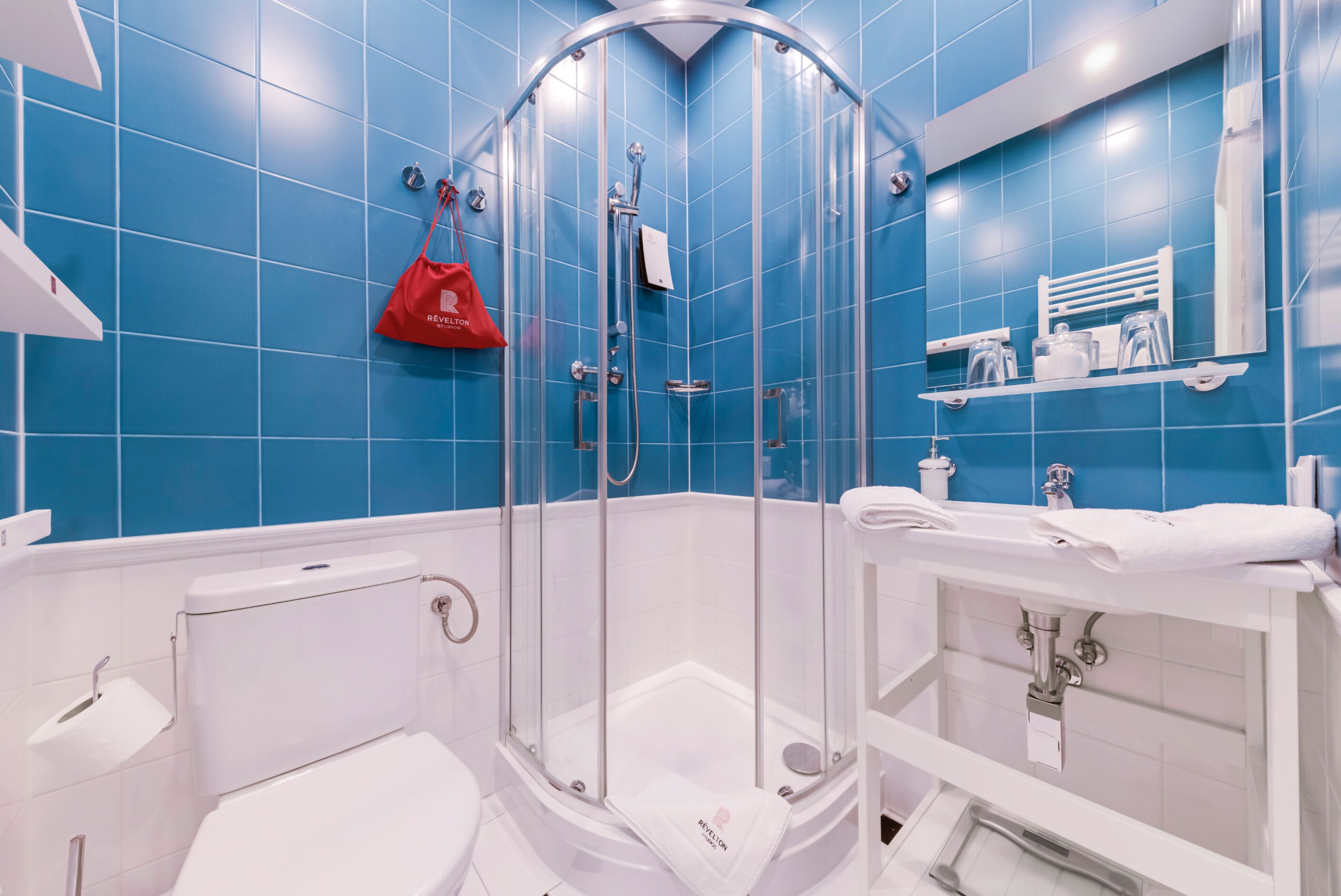 Une salle de bain moderne avec une douche à parois de verre, des éléments d’équipement blancs et des murs recouverts de carreaux bleus.