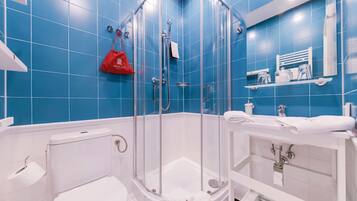 Une salle de bain moderne avec une douche à parois de verre, des éléments d’équipement blancs et des murs recouverts de carreaux bleus.