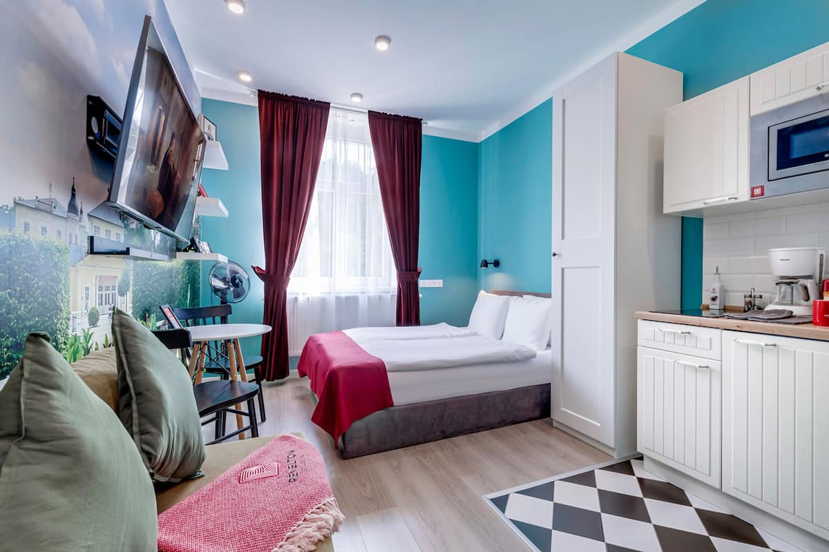 Kompakti hotellihuone, jossa on sänky, työpöytä, pieni keittiö ja ikkunasta avautuva näkymä kaupungin ylle.