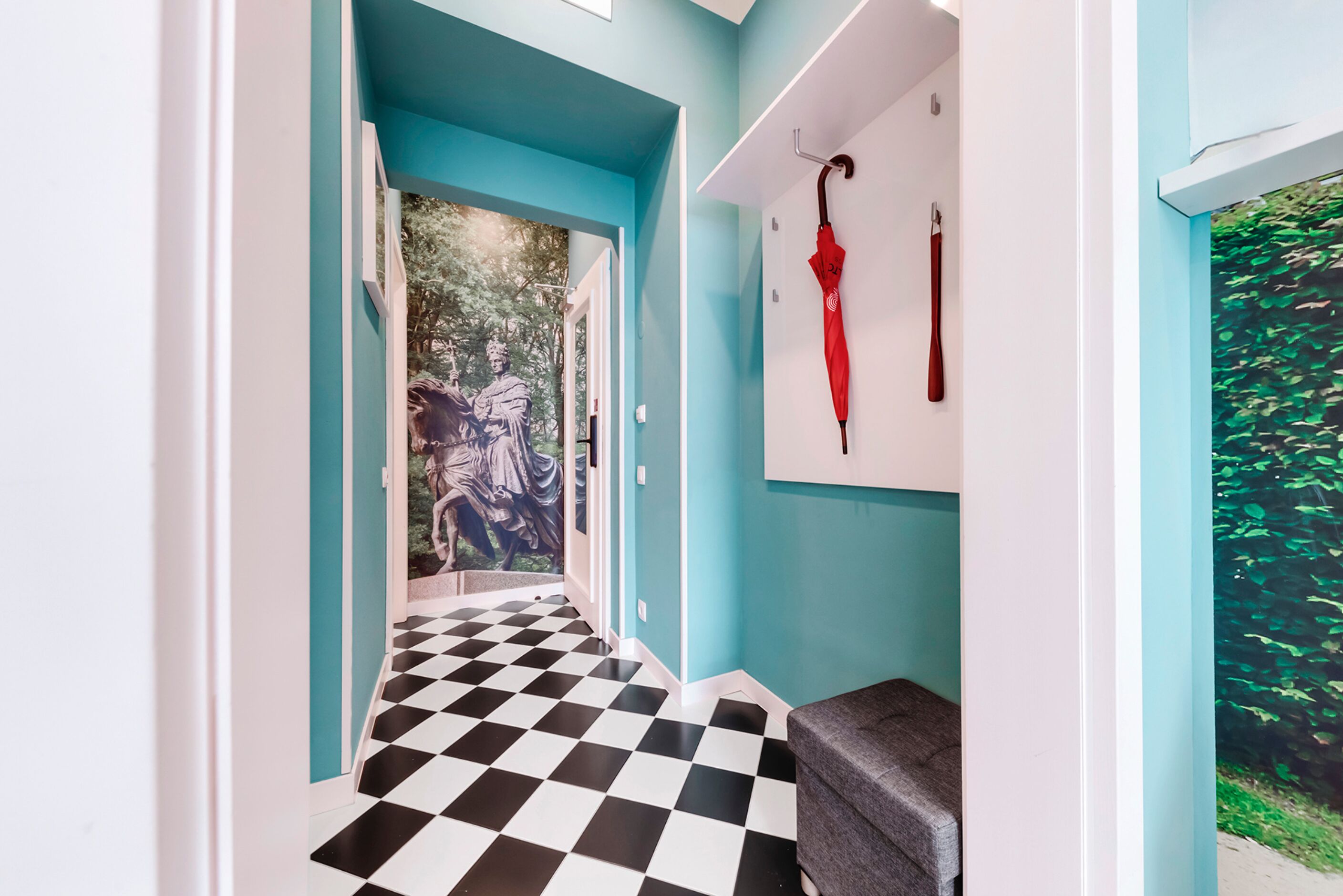 Een gang met een zwart-wit geruit vloertapijt, een blauwe muur en een deur die naar een kamer leidt met een muurschildering.