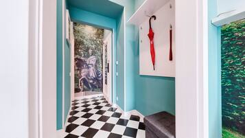 Een gang met een zwart-wit geruit vloertapijt, een blauwe muur en een deur die naar een kamer leidt met een muurschildering.
