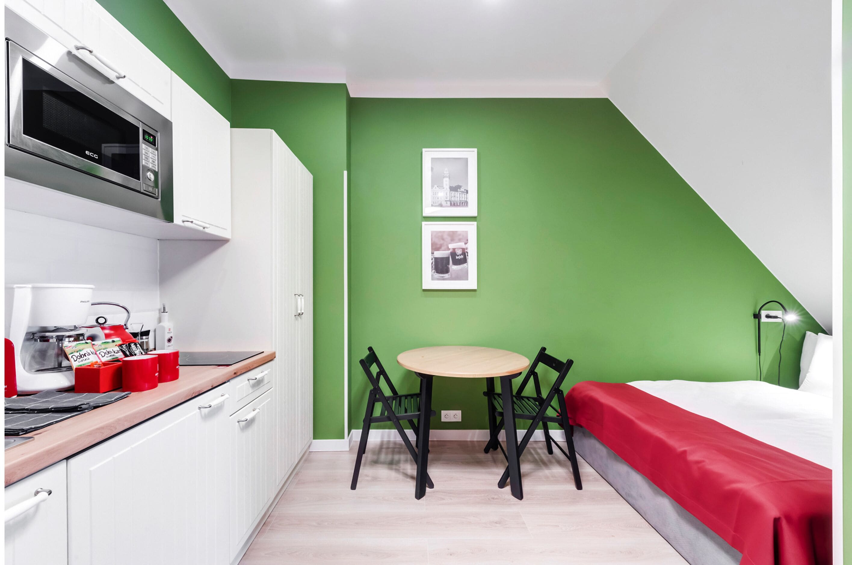 A compact room with a kitchenette, a bed, a dining table, and two framed pictures on the wall.