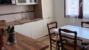 Una cocina con armarios blancos, microondas, pileta y comedor con mesa y sillas.