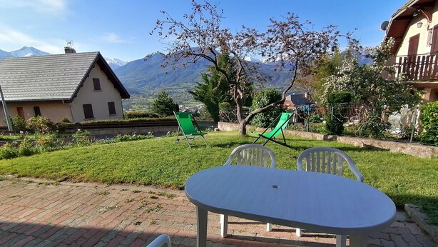 Un patio con una mesa y sillas, un área verde y vistas a la montaña.