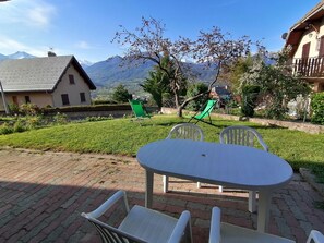 A patio with a table and chairs, a grassy area, and a mountain view. - First floor of a detached house; beautiful view (Embrun)