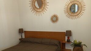 Un dormitorio con una cama grande, dos espejos en la pared, una mesita de noche con una lámpara, una pequeña mesa con una planta y una alfombra estampada.