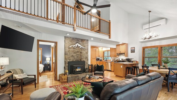A spacious living area with a fireplace, leather sofas, a dining table, and a kitchen in the background. - Guest Favorite Mt. Hood Cabin - Private Hot Tub - Sandy River (Rhododendron)