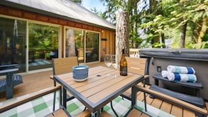 An outdoor patio with a wooden table, chairs, and a bottle of wine. - Guest Favorite Mt. Hood Cabin - Private Hot Tub - Sandy River (Rhododendron)