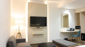 A modern hotel room with a flat-screen TV, a desk with a chair, a sofa, and a small table. - Cordia Hotel Banjarmasin - Hotel Dalam Bandara (Banjarbaru)