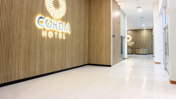 A hotel reception area with a wooden panel wall and a sign that reads "CORDIA HOTEL." - Cordia Hotel Banjarmasin - Hotel Dalam Bandara (Banjarbaru)