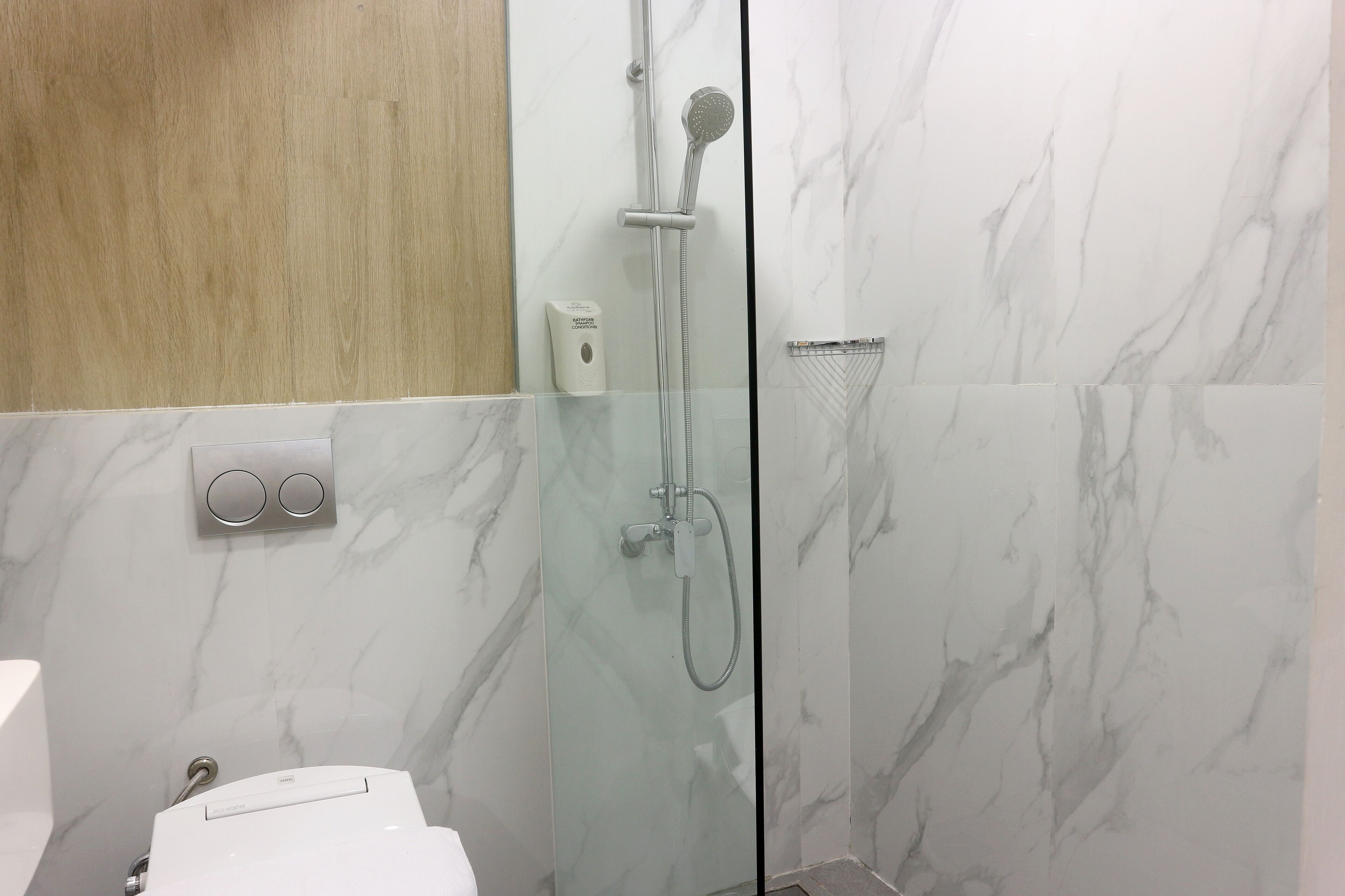 Un baño moderno con ducha envuelta en vidrio, paredes de mármol y un panel de madera sobre el espejo.