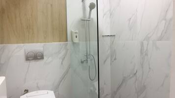 Un baño moderno con ducha envuelta en vidrio, paredes de mármol y un panel de madera sobre el espejo.