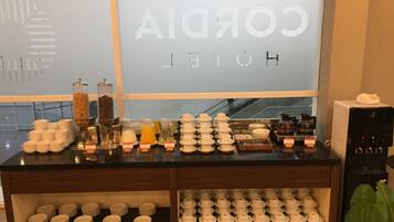 A hotel reception area with a coffee station, tea station, and a display of white cups and plates.