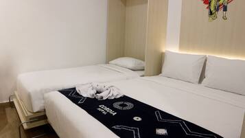 Habitación de hotel con dos camas individuales, un corredor de cama blanco y negro con el nombre del hotel, una toalla blanca en el suelo y una obra de arte colgada en la pared.