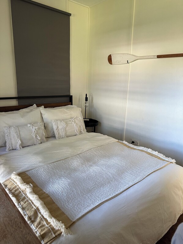 Een net opgemaakt bed met witte lakens en een decoratieve plaid, een bedlamp en een wandlamp.