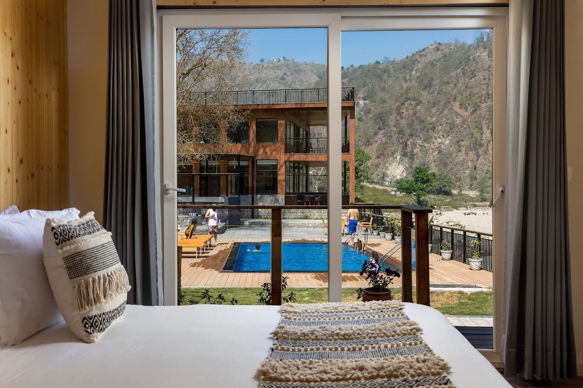 Een slaapkamer met een groot bed, uitzicht op een zwembad en een terras, en een berg op de achtergrond.