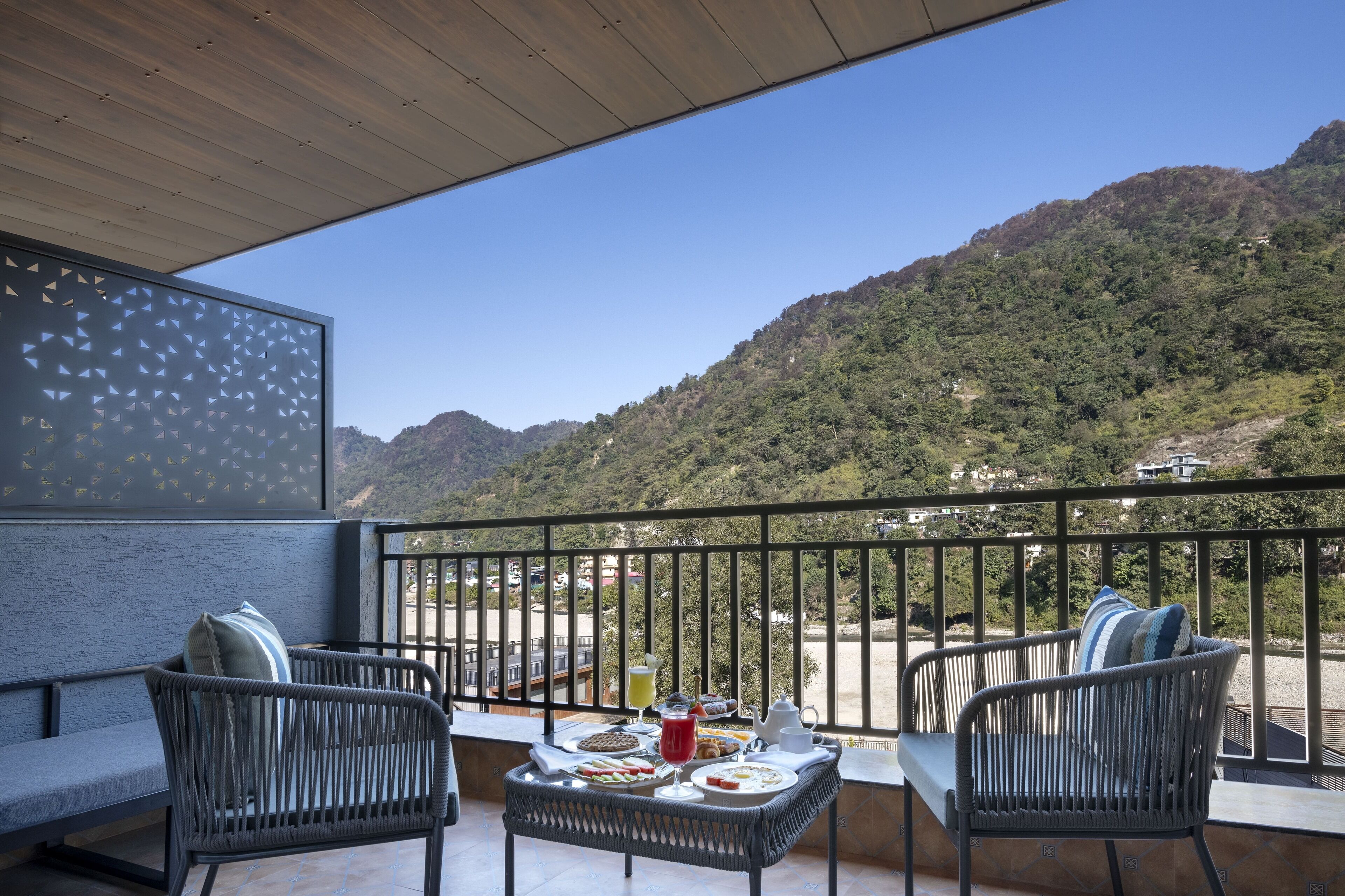 A balcony with wicker chairs and a table set with breakfast. The balcony overlooks a mountainous landscape.