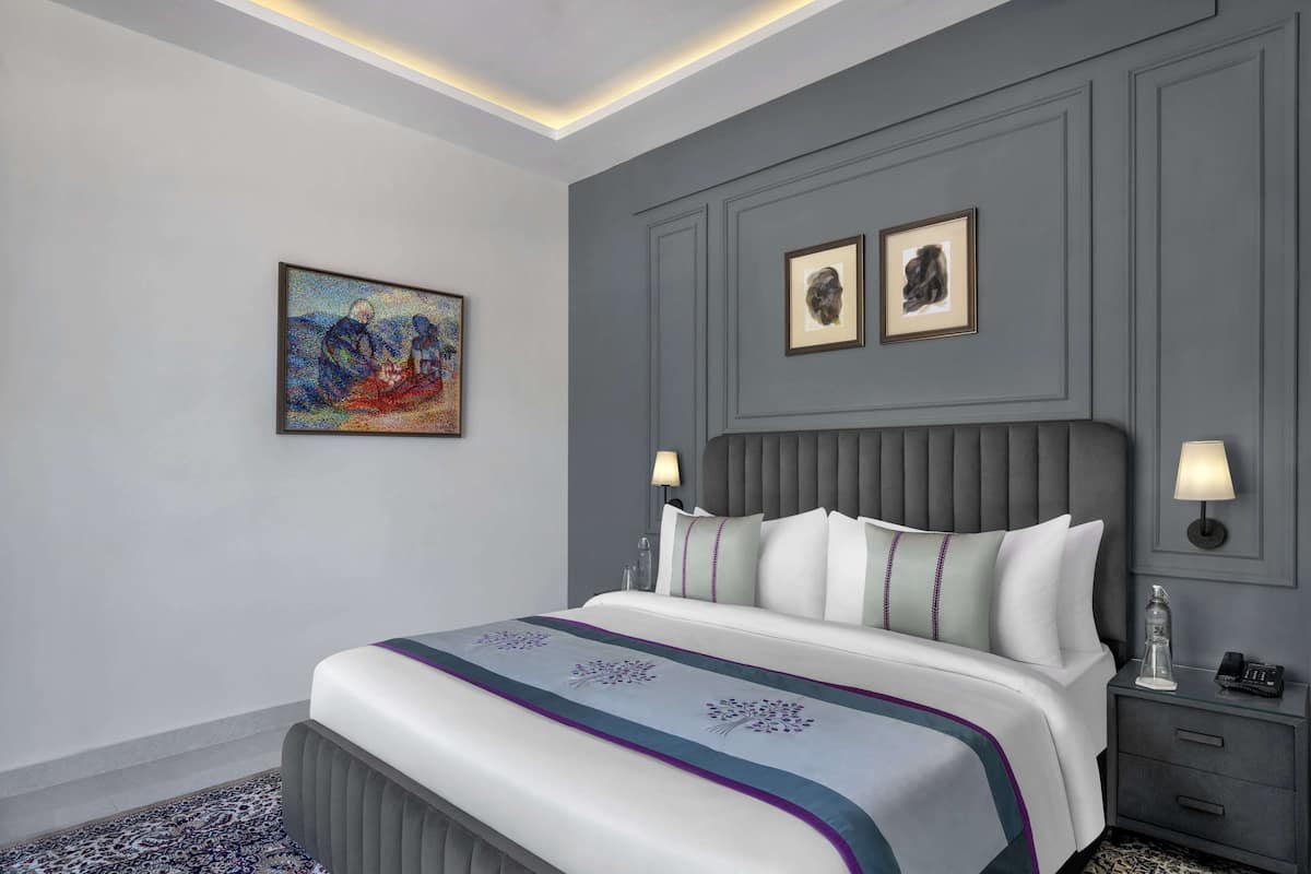 Een moderne hotelkamer met een groot bed, een hoofdeinde met ingebouwde verlichting, een nachtkastje met een lamp en een lijst aan de muur.