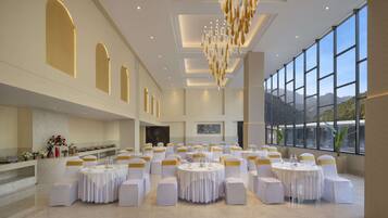 A spacious banquet hall with round tables, white chairs with gold sashes, and a large chandelier.