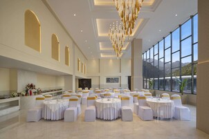 A spacious banquet hall with round tables, white chairs with gold sashes, and a large chandelier.