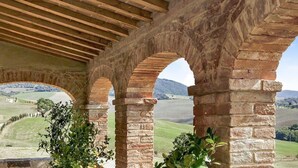 Un arc en pierre surmonté d’un plafond en bois, qui mène à un point de vue sur un paysage rural.