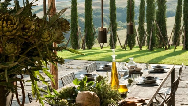 Un espace de restauration en plein air avec une table en pierre prévue pour deux personnes, entourée de verdure et offrant une vue panoramique sur des collines ondulantes.
