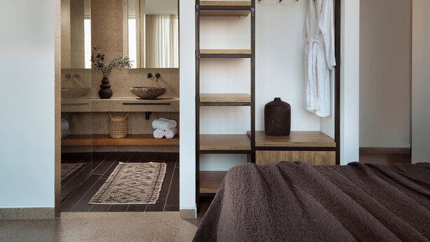 Een moderne badkamer met een grote spiegel, een stenen wastafel en een houten plank met handdoeken en een vaas.