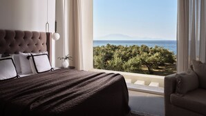 Une chambre avec un grand lit, une vue sur la mer et un balcon donnant sur les arbres.