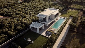 Une maison moderne avec une piscine, entourée d’une végétation luxuriante et avec des collines en arrière-plan.