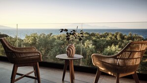 Un balcon agrémenté de fauteuils en osier et d’une petite table, offrant une vue panoramique sur la mer et la verdure.