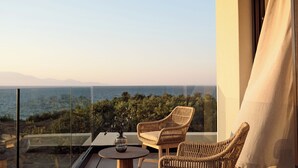 Un balcon agrémenté de fauteuils en osier et d’une petite table ronde, offrant une vue panoramique sur la mer et les montagnes lointaines.