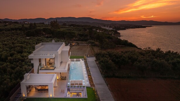 Une maison moderne avec une piscine, offrant une vue sur un plan d’eau et des montagnes.