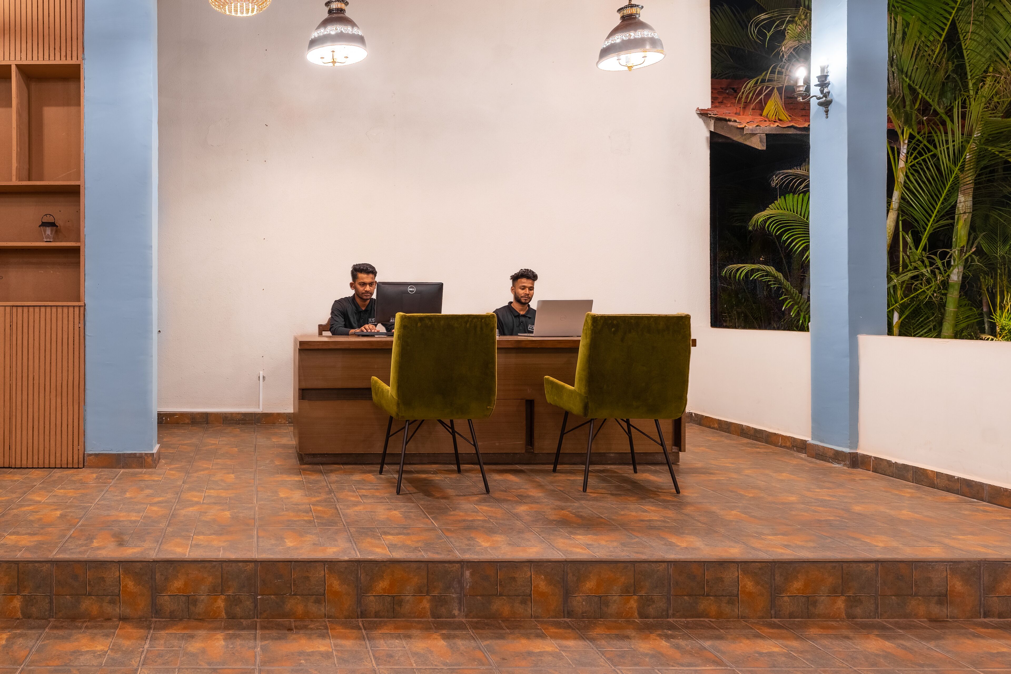 Un área de recepción con dos personas sentadas en un escritorio, un armario de madera y suelo de baldosas.