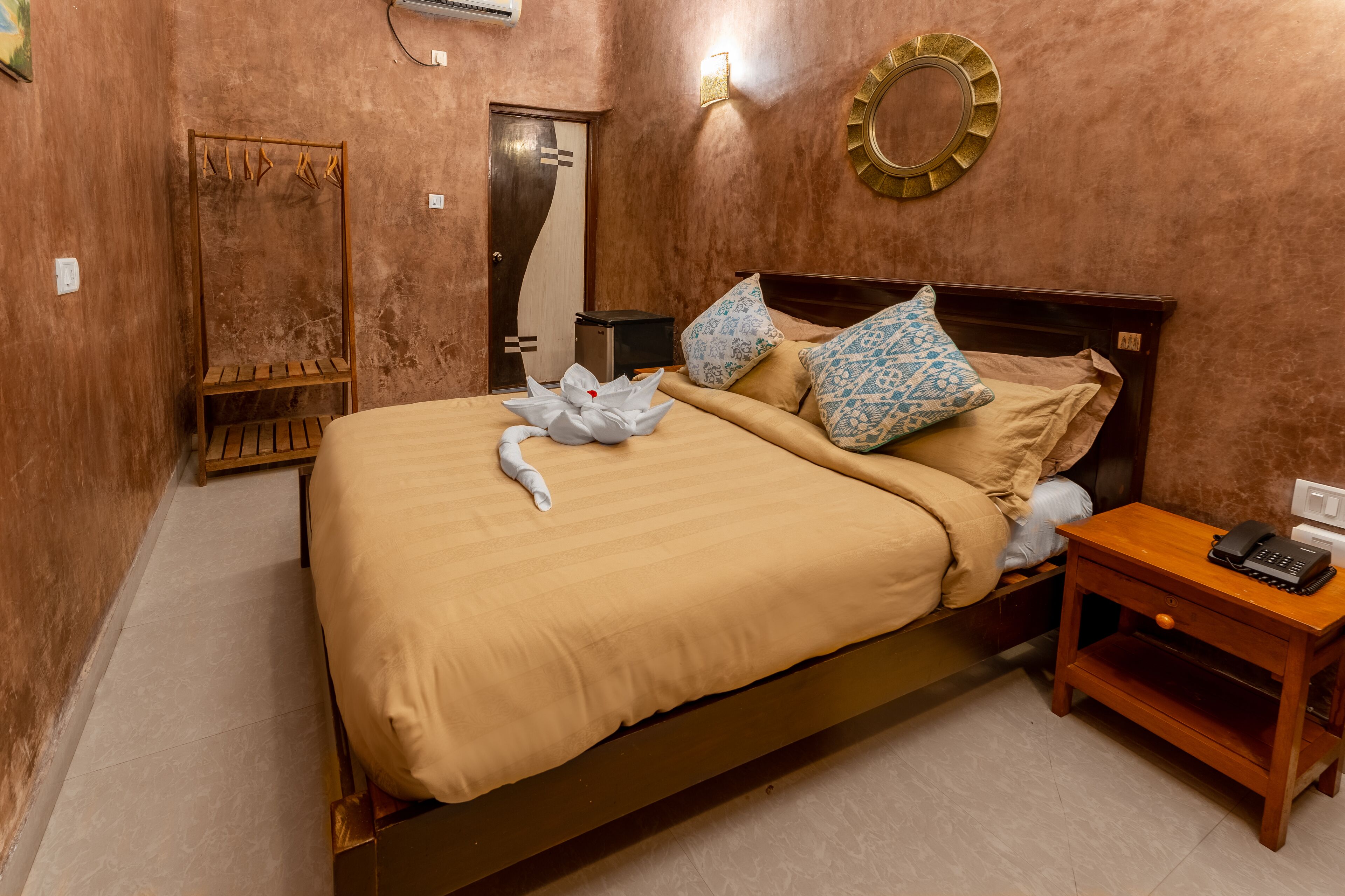 A neatly made bed with a beige comforter, two patterned pillows, and a white towel with a bow.